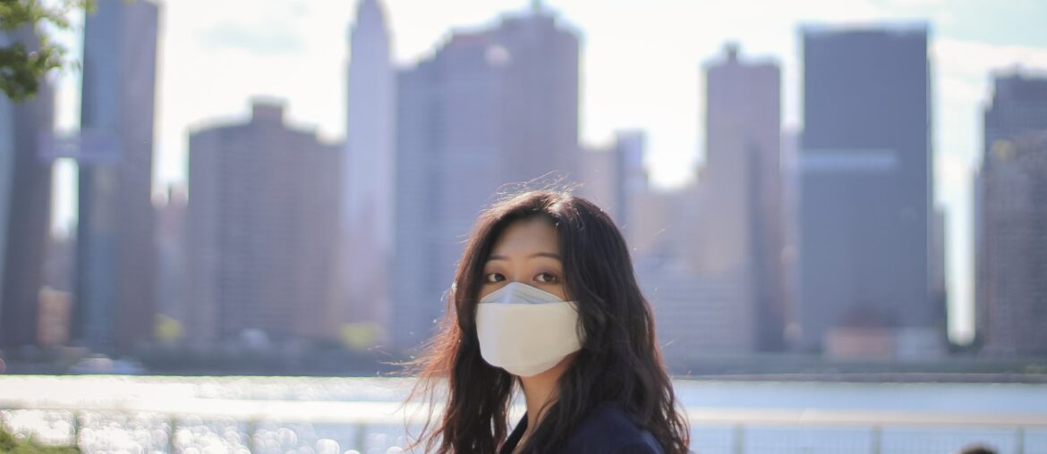 Woman wearing mask in front of New York City skyline on a clear, sunny day