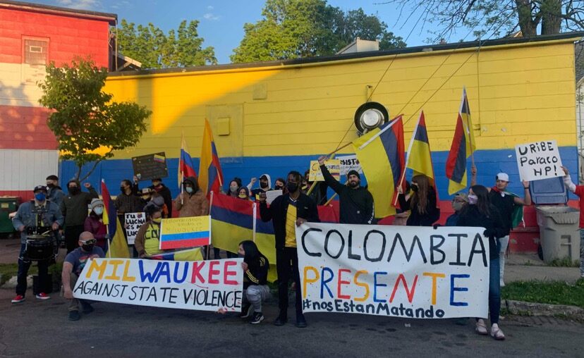 Protestors holding up Colombian flags and signs. One says, “Milwaukee Against State Violence” and the other sign says “Colombia Presente #nos estan matando” which translates to “They’re killing us.”