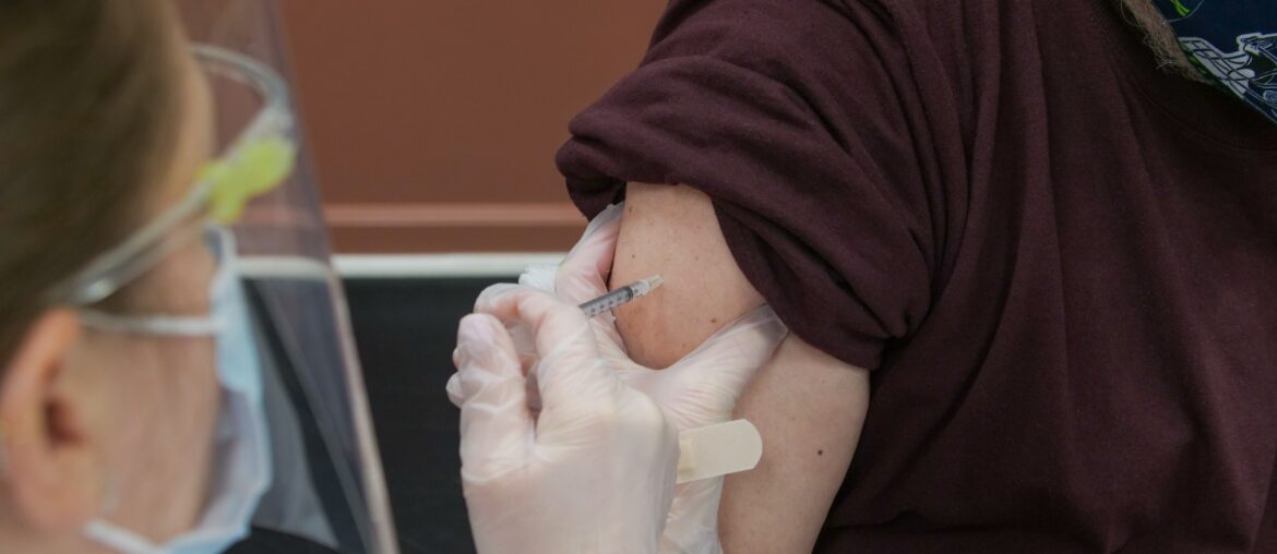 A health worker with a face shield and gloves is administering a vaccine to a man's right arm