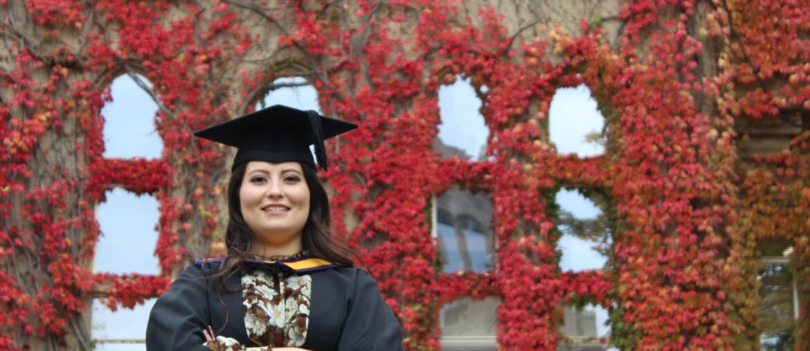Woman in graduation robes standing in front of brick building covered in ivy