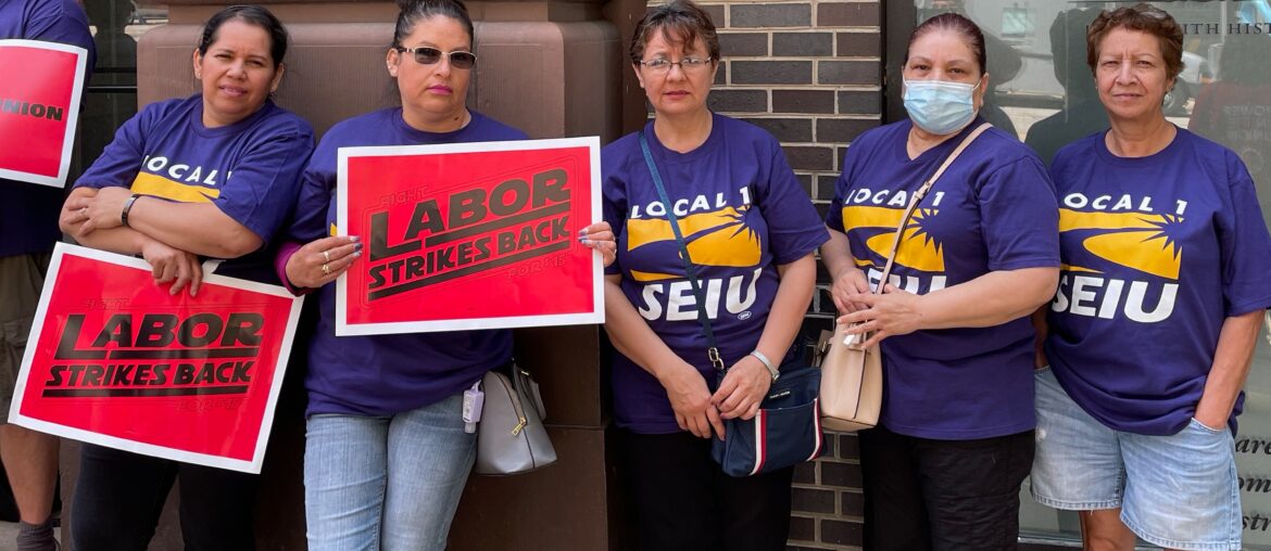 Women wearing SEIU t-shirts are holding up signs that say "Labor Strikes Back"