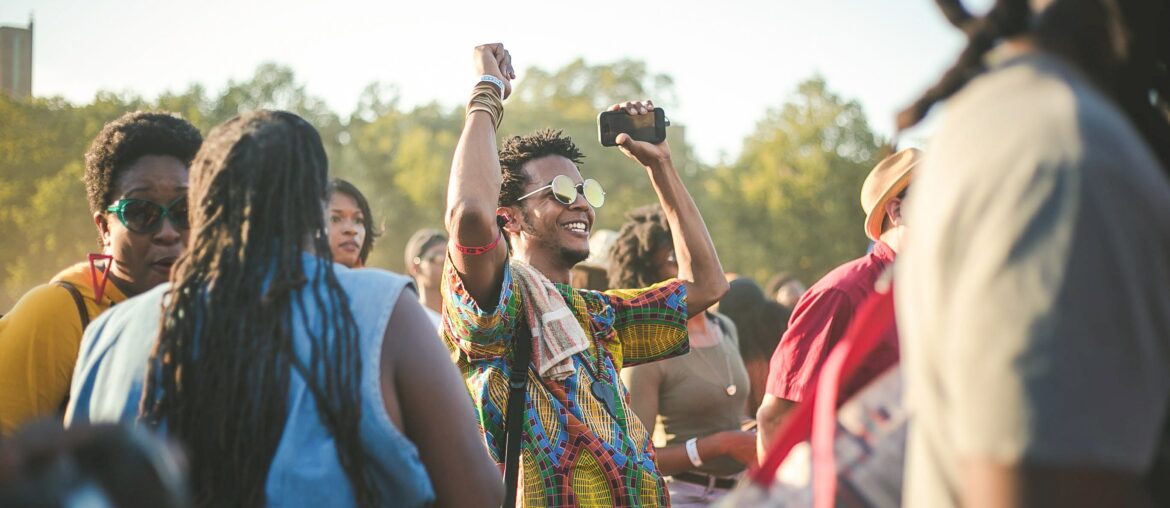 Man wearing sunglasses smiling with arms up, celebrating in a crowd