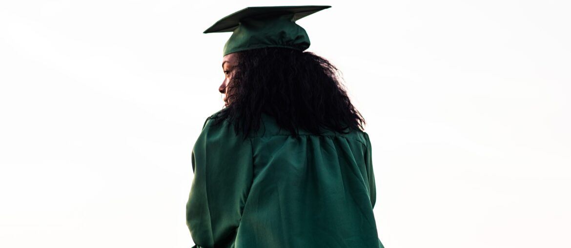 woman wearing graduation cap and gown looks over her left shoulder