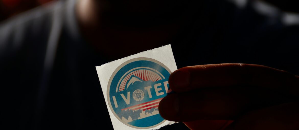 a hand is holding up a circle-shaped sticker that says "I voted"
