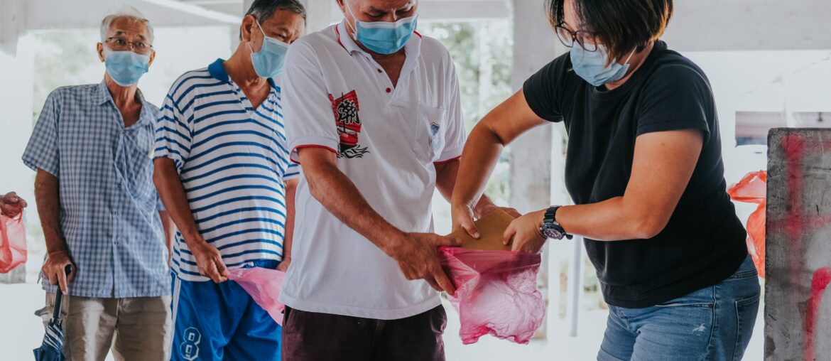 People wearing masks are in line while a man in front is getting food placed in his plastic bag