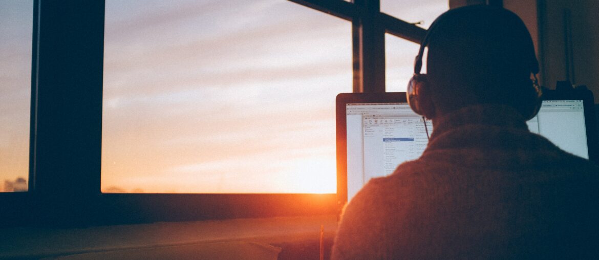 Person with headphones on looking at computer with sunrise coming in through the window
