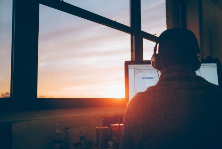 Person with headphones on looking at computer with sunrise coming in through the window