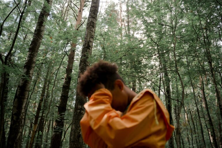 Teenage boy in yellow-raincoat with head in hands in forest