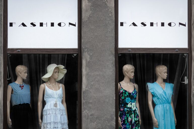 Mannequins in a storefront with the words "Fashion" written on the awning